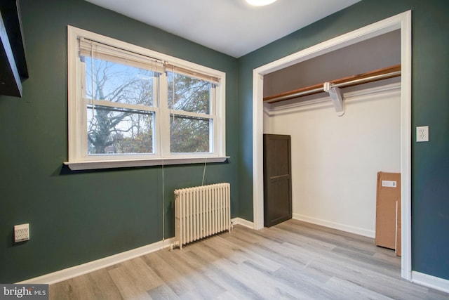 unfurnished bedroom with radiator heating unit, light wood-type flooring, and a closet