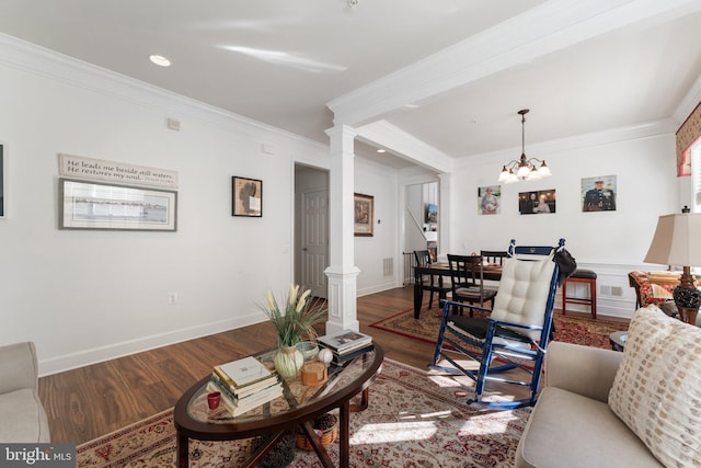 living room featuring wood-type flooring, crown molding, a chandelier, and decorative columns