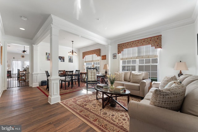 living room featuring dark wood-type flooring, ornate columns, ornamental molding, and ceiling fan with notable chandelier