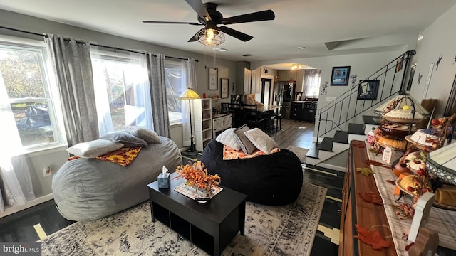 living room featuring arched walkways, ceiling fan, wood finished floors, baseboards, and stairs