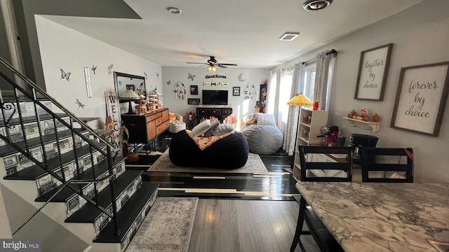 living area featuring a ceiling fan, wood finished floors, visible vents, and stairs