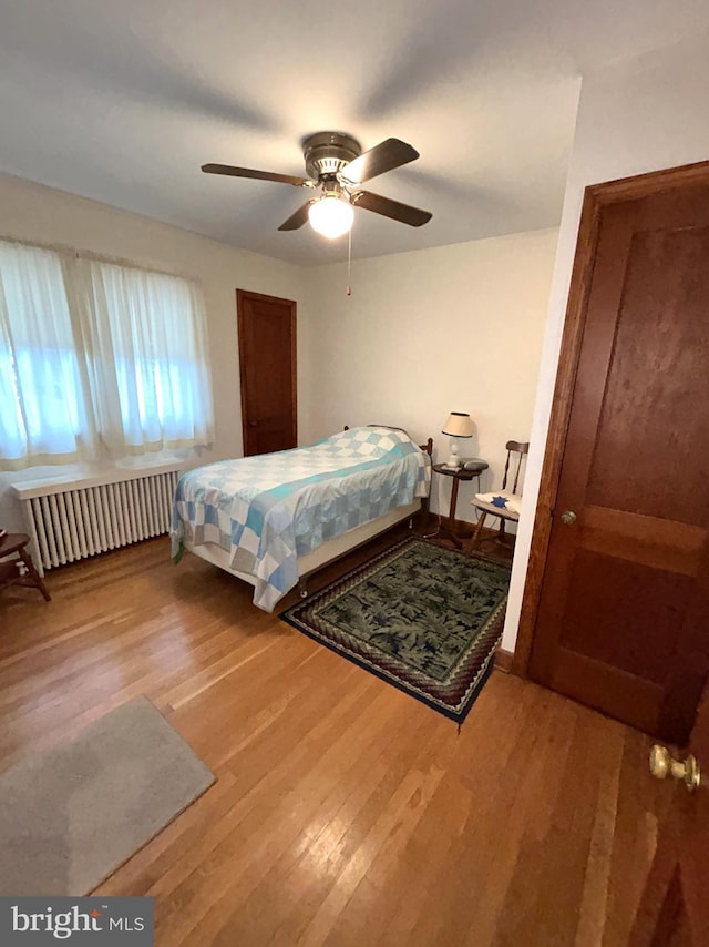 bedroom featuring ceiling fan, radiator heating unit, and wood-type flooring