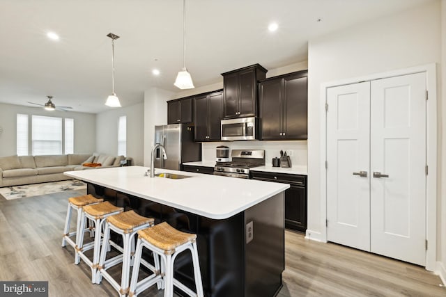 kitchen featuring a center island with sink, sink, hanging light fixtures, appliances with stainless steel finishes, and a breakfast bar area