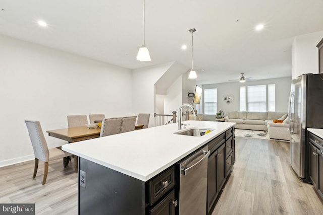 kitchen featuring sink, hanging light fixtures, stainless steel appliances, light hardwood / wood-style floors, and a kitchen island with sink