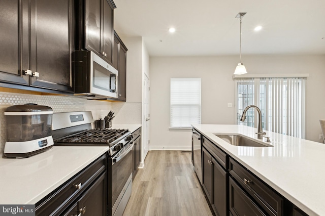 kitchen featuring tasteful backsplash, stainless steel appliances, sink, decorative light fixtures, and light hardwood / wood-style floors