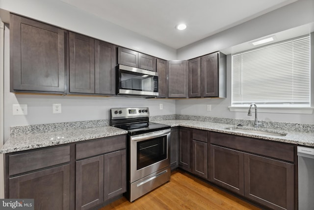 kitchen with dark brown cabinetry, sink, stainless steel appliances, light stone counters, and light hardwood / wood-style floors