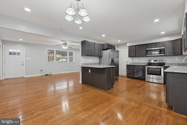 kitchen with light stone countertops, a center island, hanging light fixtures, stainless steel appliances, and light wood-type flooring