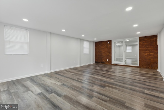 unfurnished living room with a wealth of natural light, brick wall, and dark hardwood / wood-style floors