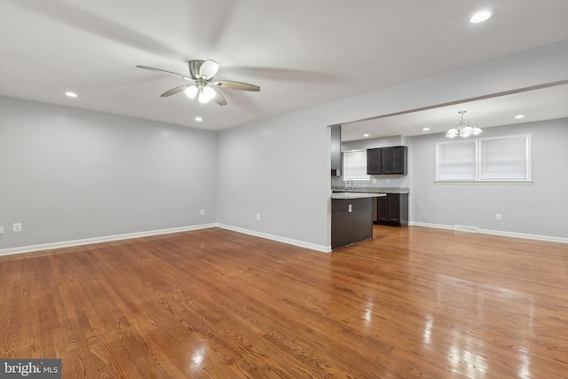 unfurnished living room featuring ceiling fan with notable chandelier and light wood-type flooring