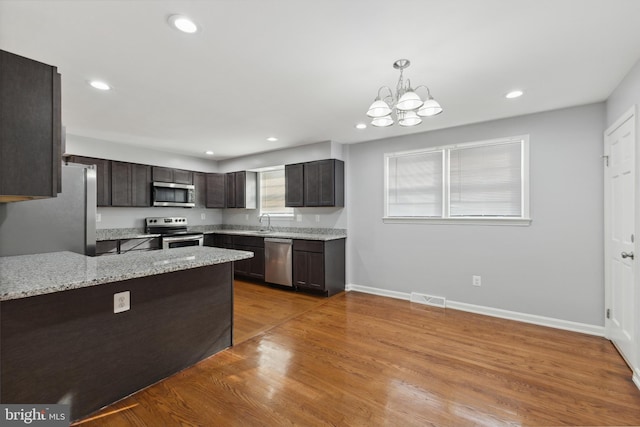 kitchen featuring light wood-type flooring, dark brown cabinets, stainless steel appliances, decorative light fixtures, and an inviting chandelier