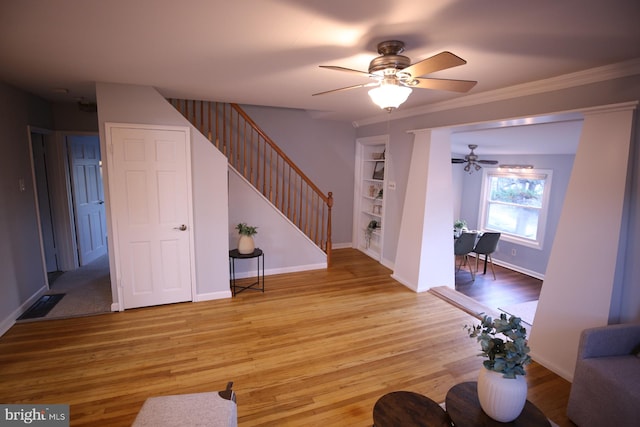 living room with built in shelves, light hardwood / wood-style flooring, ceiling fan, and crown molding