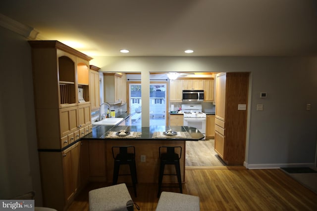 kitchen featuring white stove, sink, hardwood / wood-style flooring, a kitchen bar, and kitchen peninsula