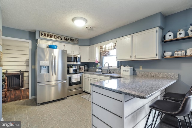 kitchen with kitchen peninsula, a textured ceiling, stainless steel appliances, sink, and white cabinets