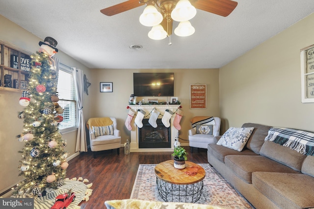 living room with a textured ceiling, ceiling fan, and dark wood-type flooring