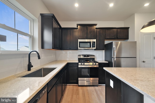 kitchen featuring light stone countertops, sink, stainless steel appliances, light hardwood / wood-style flooring, and backsplash