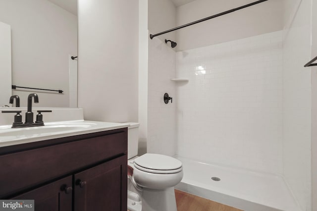 bathroom with hardwood / wood-style flooring, vanity, toilet, and tiled shower