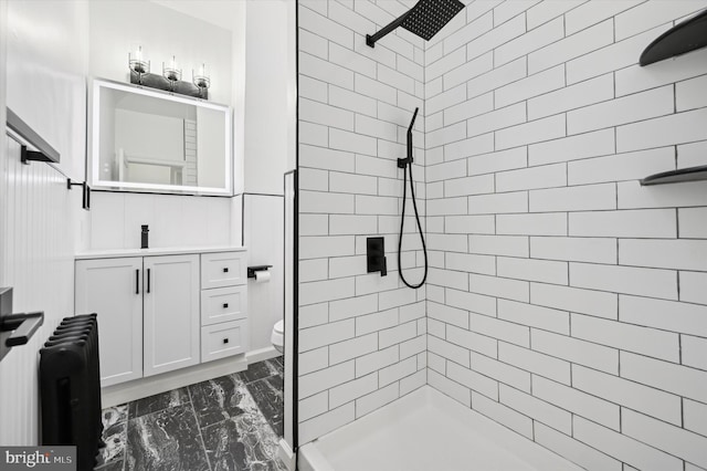 bathroom featuring vanity, toilet, tiled shower, and radiator