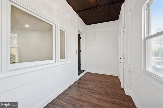 hallway with dark hardwood / wood-style floors and brick wall