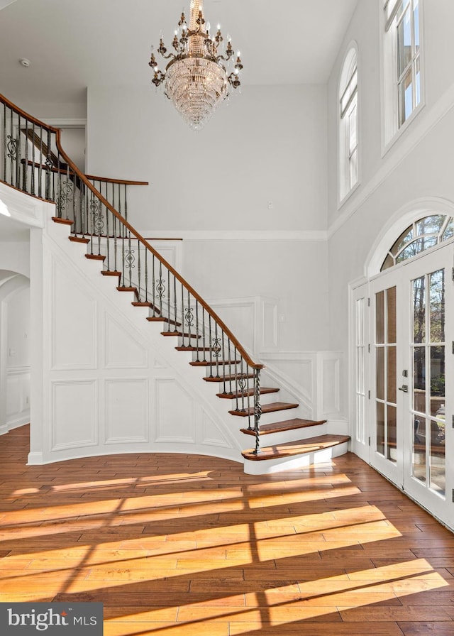 entryway featuring hardwood / wood-style floors, a towering ceiling, french doors, and a notable chandelier