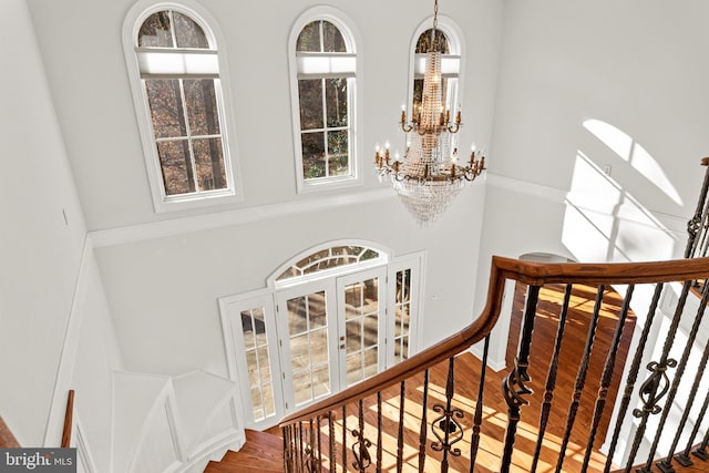 staircase with a chandelier, wood-type flooring, and a towering ceiling