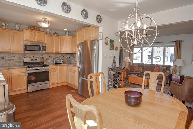 kitchen with appliances with stainless steel finishes, backsplash, light brown cabinetry, an inviting chandelier, and dark hardwood / wood-style floors