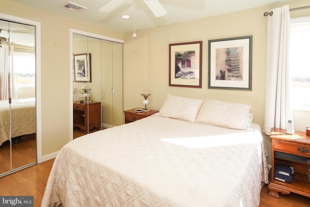 bedroom with multiple windows, ceiling fan, wood-type flooring, and multiple closets