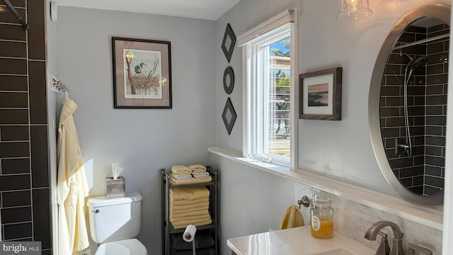 bathroom with tiled shower, toilet, sink, and a wealth of natural light