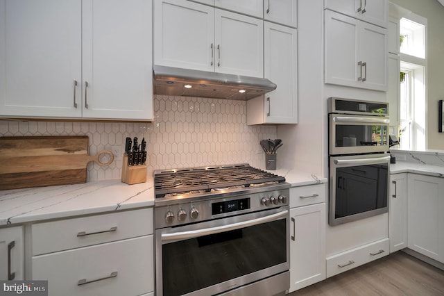 kitchen featuring white cabinetry, stainless steel appliances, tasteful backsplash, light stone counters, and light hardwood / wood-style floors