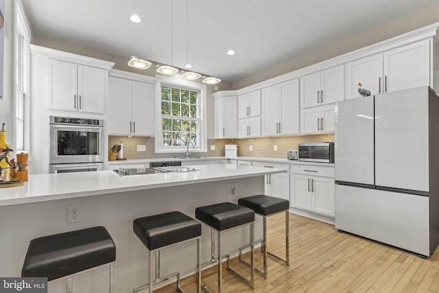 kitchen with a kitchen bar, appliances with stainless steel finishes, backsplash, white cabinets, and light hardwood / wood-style floors