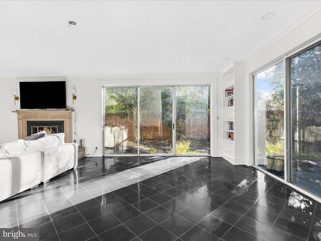 unfurnished living room featuring a healthy amount of sunlight, built in features, crown molding, and dark tile patterned floors