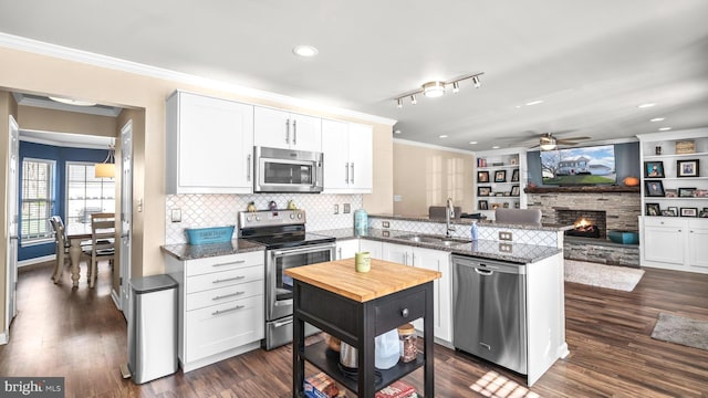 kitchen featuring white cabinetry, sink, stainless steel appliances, a stone fireplace, and kitchen peninsula