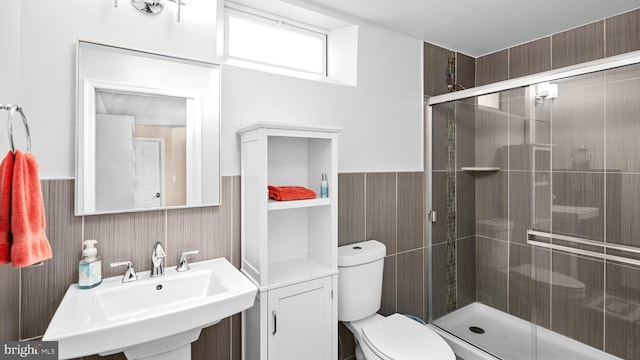 bathroom featuring toilet, a shower with shower door, and sink