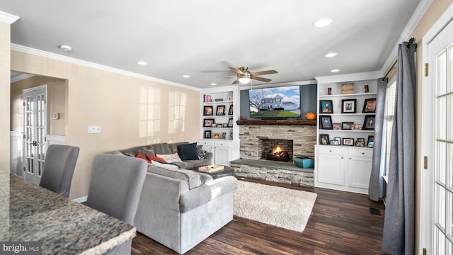 living room featuring built in shelves, ceiling fan, dark wood-type flooring, crown molding, and a fireplace