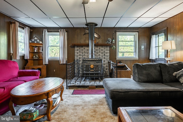 living room featuring light colored carpet, a wood stove, ceiling fan, and wood walls