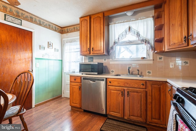 kitchen featuring sink, light wood-type flooring, a textured ceiling, appliances with stainless steel finishes, and tasteful backsplash