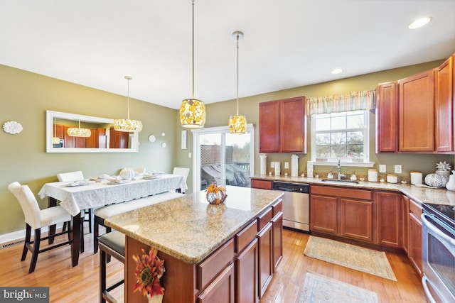 kitchen featuring light stone counters, stainless steel appliances, sink, decorative light fixtures, and light hardwood / wood-style floors