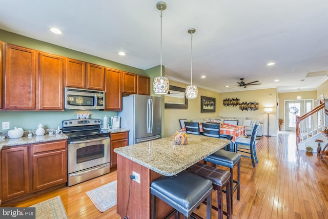 kitchen featuring a breakfast bar, hanging light fixtures, light hardwood / wood-style flooring, light stone countertops, and stainless steel appliances