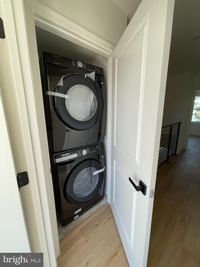 laundry room featuring stacked washing maching and dryer and light hardwood / wood-style flooring