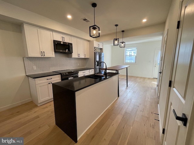 kitchen featuring stainless steel appliances, pendant lighting, a center island with sink, white cabinets, and light hardwood / wood-style floors