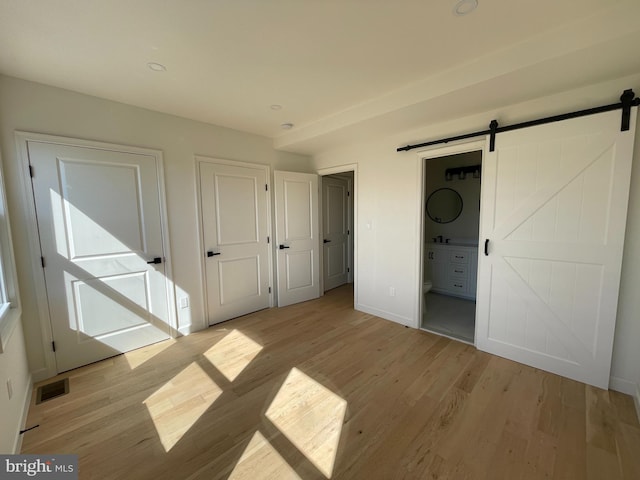 unfurnished bedroom featuring a barn door, connected bathroom, and light hardwood / wood-style flooring