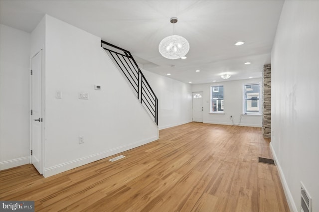 unfurnished living room with an inviting chandelier and light wood-type flooring