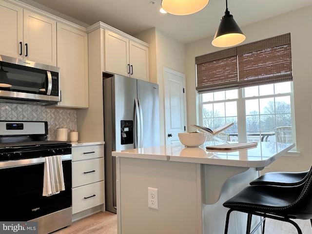 kitchen featuring hanging light fixtures, appliances with stainless steel finishes, decorative backsplash, white cabinets, and light wood-type flooring