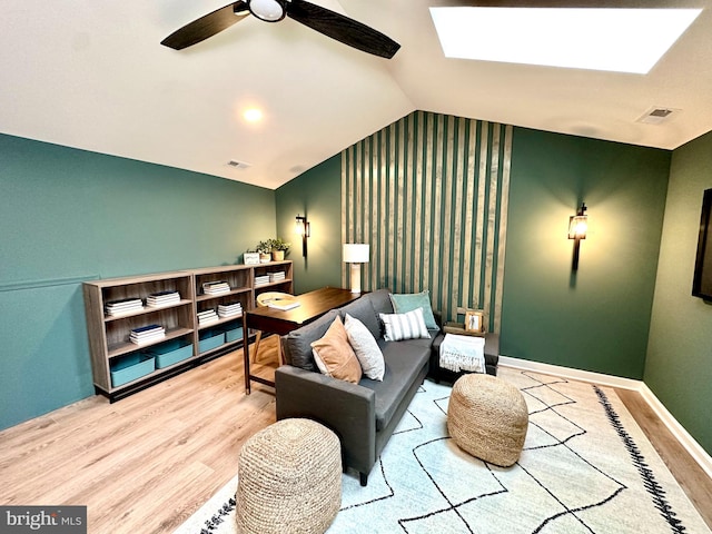 living area with vaulted ceiling with skylight, ceiling fan, and light hardwood / wood-style floors