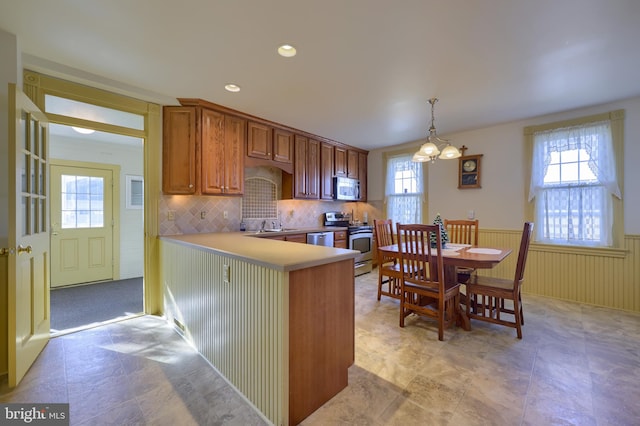 kitchen with kitchen peninsula, appliances with stainless steel finishes, a wealth of natural light, and hanging light fixtures