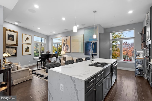 kitchen featuring light stone countertops, decorative light fixtures, a wealth of natural light, and a kitchen island with sink