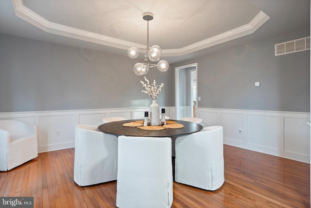 dining area featuring a chandelier, wood-type flooring, a raised ceiling, and ornamental molding