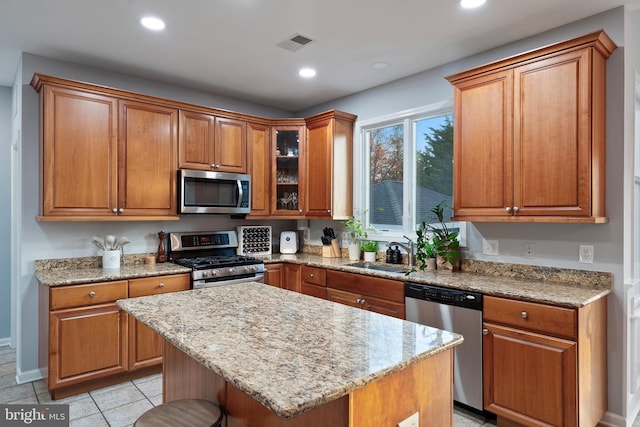 kitchen with sink, light stone countertops, appliances with stainless steel finishes, a kitchen island, and a kitchen bar