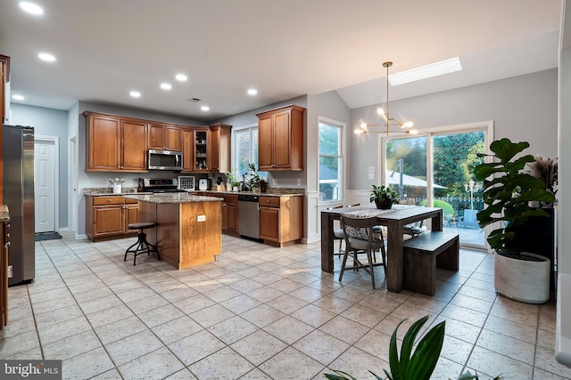 kitchen with a center island, a skylight, light stone countertops, appliances with stainless steel finishes, and a kitchen bar