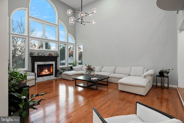 living room featuring hardwood / wood-style flooring, a premium fireplace, a towering ceiling, and a chandelier