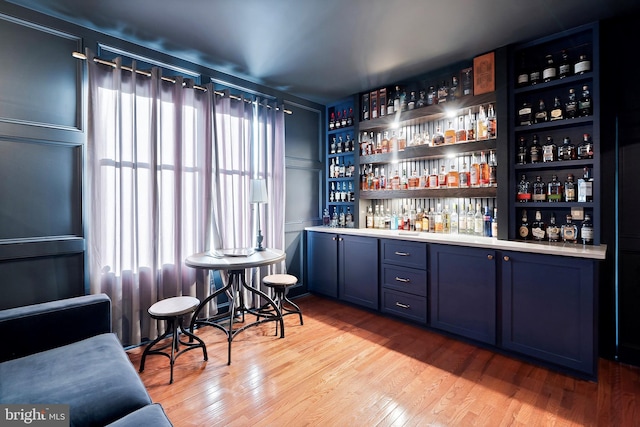 bar with blue cabinetry and light wood-type flooring